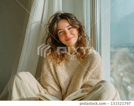 Woman smiling by window with book enjoying cozy moment 131521797