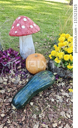 Autumn garden arrangement with pumpkin, zucchini, yellow flowers and painted mushroom decoration on grass. Concept of seasonal decor, harvest celebration and countryside charm 131521825