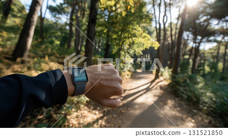 Person wearing smartwatch checking stats while running along sunlit forest trail in the morning. Concept of healthy lifestyle, fitness tracking and nature-focused wellbeing 131521850