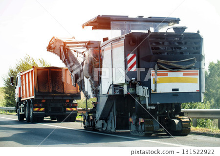 A special road-cutting machine, specifically designed for cutting asphalt layers, cuts asphalt into a dump truck with asphalt chips. Country road repair. Copy space for text A special road-cutting machine, specifically designed for cutting asphalt layers, cuts asphalt into a dump truck with asphalt chips. Country road repair. Copy space for text 131522922