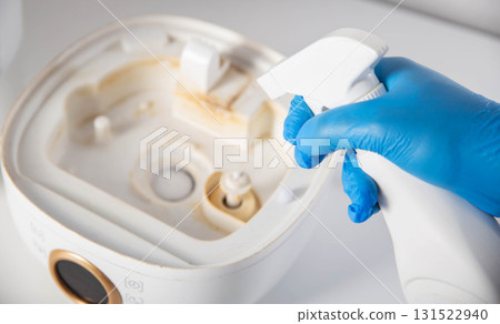 Man in blue gloves spraying descaler, mold and odor remover into humidifier on white background. Humidifier device maintenance concept. 131522940
