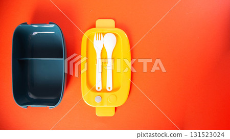 Modern lunch box for storing food on orange background. Concept set of box fork and spoon, close-up. Copy space for text Modern lunch box for storing food on orange background. Concept set of box fork and spoon, close-up. Copy space for text 131523024