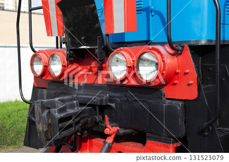 Engine front view showing details of a colorful locomotive near a grassy area in bright daylight Engine front view showing details of a colorful locomotive near a grassy area in bright daylight 131523079