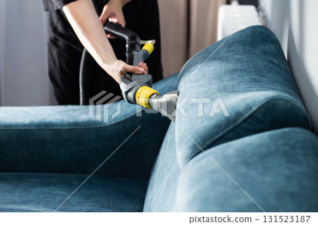 Cleaning a blue couch with a vacuum cleaner in a bright living room while maintaining a tidy home environment Cleaning a blue couch with a vacuum cleaner in a bright living room while maintaining a tidy home environment 131523187
