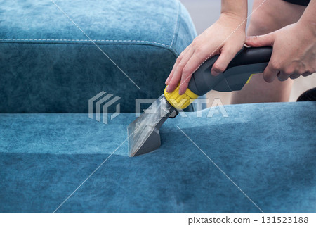 Cleaning upholstery on a blue sofa in a sunlit room with a professional tool for deep cleaning 131523188