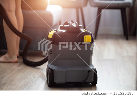 A modern upholstery vacuum cleaner stands in a room against a sunset backdrop. Cleaning service, industry A modern upholstery vacuum cleaner stands in a room against a sunset backdrop. Cleaning service, industry 131523193
