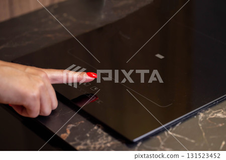 A finger with a red manicure sets the temperature on a ceramic hob, close-up. Copy space for text 131523452
