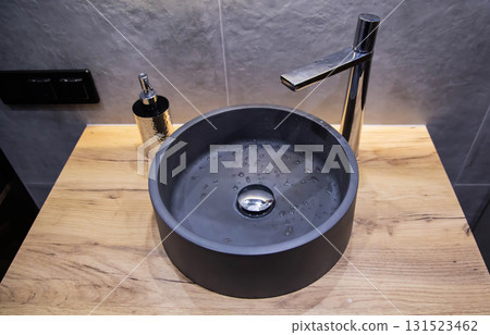 Stylish modern gray stone sink in the bathroom in a suspended wooden cabinet and a chrome tap. Gray tiles on the wall, interior 131523462