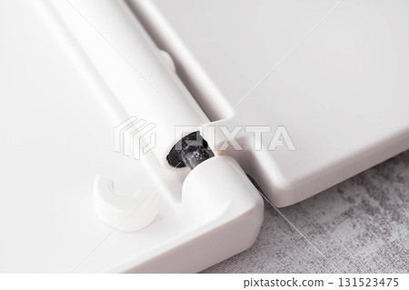 Broken hinge of a white toilet seat, close-up, low-quality plastic, industry Broken hinge of a white toilet seat, close-up, low-quality plastic, industry 131523475