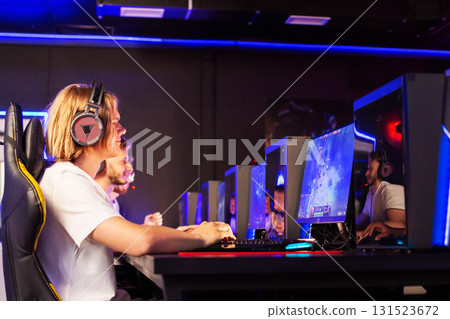 Young gamers competing in an esports tournament at an entertainment venue with glowing screens and high-tech equipment Young gamers competing in an esports tournament at an entertainment venue with glowing screens and high-tech equipment 131523672