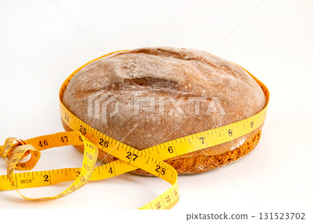 A round loaf of bread is wrapped in a yellow measuring tape on a white background. 131523702