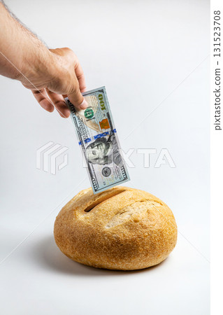 A loaf of bread with a coin slot. A man's hand inserts a hundred-dollar bill 131523708