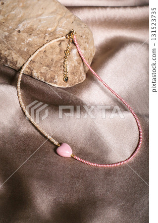 Unique costume jewelry necklace with pink heart pendant rests on soft silk fabric 131523735