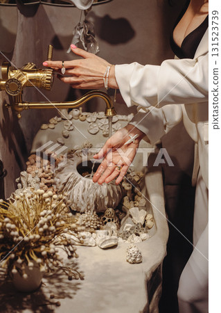 Young woman with stylish pearl beads washes hands at seashell-decorated washbasin indoors 131523739