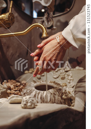 Young woman washes hands in seashell-decorated basin while wearing fashionable pearl beads Young woman washes hands in seashell-decorated basin while wearing fashionable pearl beads 131523745