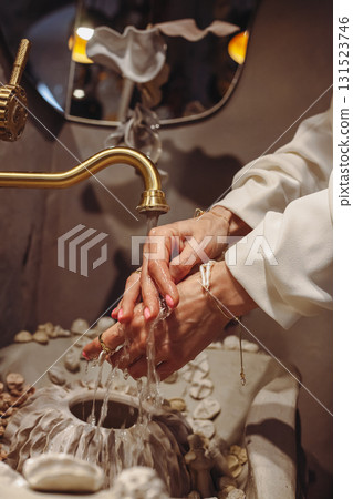 Young woman washes hands in a seashell-decorated washbasin with fashionable pearl beads Young woman washes hands in a seashell-decorated washbasin with fashionable pearl beads 131523746