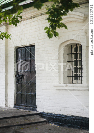 Old brick building with a black door and barred window in a quiet neighborhood 131523781