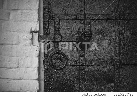 Old black iron door with padlock and ring in rustic building setting Old black iron door with padlock and ring in rustic building setting 131523783