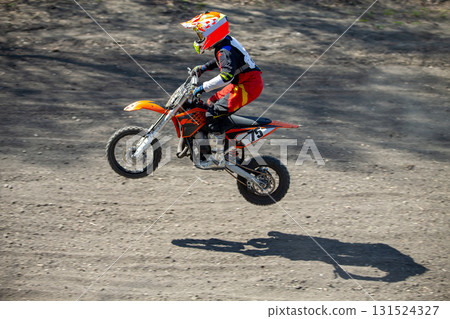 Child motocross rider performing jump on dusty track 131524327