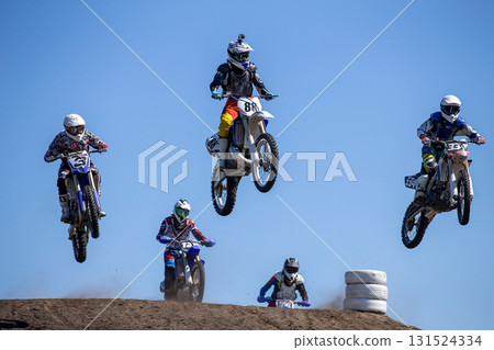 Group motocross riders performing high jump over hill 131524334