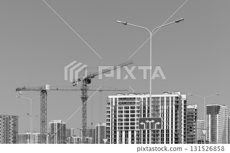 Monochrome view of construction cranes over unfinished highrise tower with steel framework in urban Monochrome view of construction cranes over unfinished highrise tower with steel framework in urban 131526858