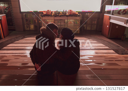A young couple in love is sitting in a street cinema and looking at each other, hugging and kissing against the background of the screen 131527817