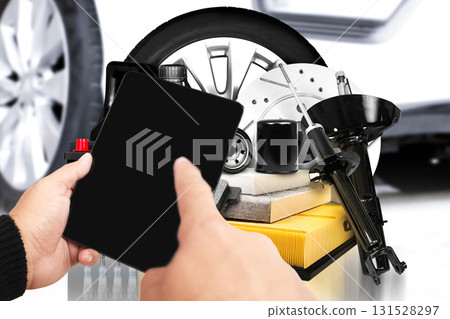 Hands holding digital tablet with black blank screen in front of car spare parts 131528297