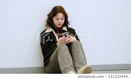 A girl leans against a wall, her smile showing the impact of a positive digital interaction. This photo highlights the blend of technology and emotions in today s connected world. A girl leans against a wall, her smile showing the impact of a positive digital interaction. This photo highlights the blend of technology and emotions in today s connected world. 131528444