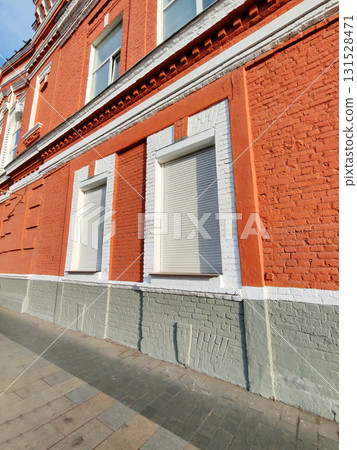 A red brick building with closed white automatic shutters on its windows, emphasizing security and safety. The image highlights modern protection solutions on classic architecture. 131528471
