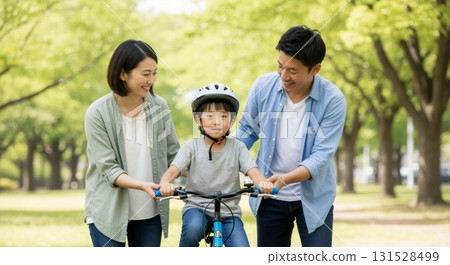 Asian parents teaching their young son how to ride a bicycle in the park. Happy family bonding and enjoying an outdoor activity together 131528499