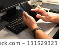 The hands of a man operating a smartphone in front of a computer 131529323