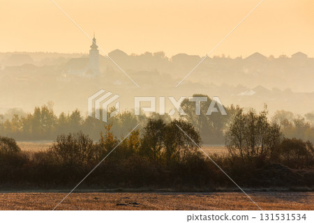 rural landscape on an autumn morning. row of trees along the empty fields. village with church on the hill behind the forest in the hazy distance rural landscape on an autumn morning. row of trees along the empty fields. village with church on the hill behind the forest in the hazy distance 131531534