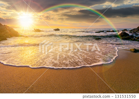 sea coast with rainbow over the boulders in the bay at sunset. sea tide with calm waves wash the golden sandy beach in evening light. beautiful autumn vacation at the seaside for honeymoon backdrop sea coast with rainbow over the boulders in the bay at sunset. sea tide with calm waves wash the golden sandy beach in evening light. beautiful autumn vacation at the seaside for honeymoon backdrop 131531550