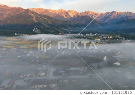 Hakuba townscape seen through a sea of clouds in the early morning, with the Hakuba Sanzan mountains shining in the morning sun. Hakuba Village, Nagano Prefecture (aerial shot by drone) 131531950