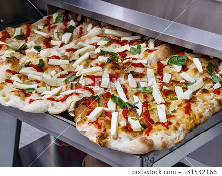 Freshly baked pizza with tomato sauce and mozzarella cheese, topped with basil, ready to serve in a busy kitchen 131532166