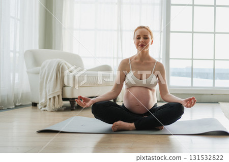 Pregnancy prenatal breathing. Pregnant woman with big belly sitting in lotus pose on yoga matt at home. Pregnant girl practicing yoga mindfulness meditation. Relaxation self care during pregnancy 131532822