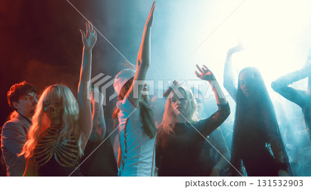Girls in Halloween costumes dancing with raised hands in smoky neon club atmosphere 131532903