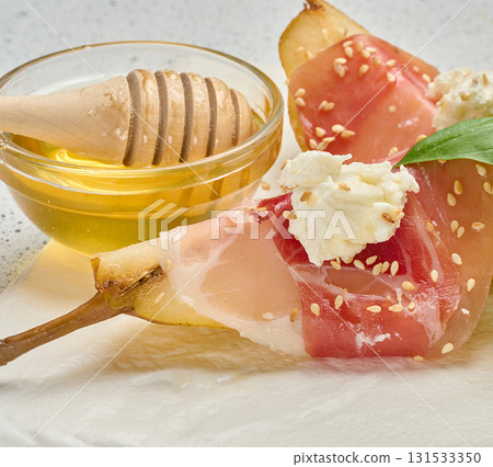 Pear slice wrapped in prosciutto with cheese and sesame seeds on a white board Pear slice wrapped in prosciutto with cheese and sesame seeds on a white board 131533350