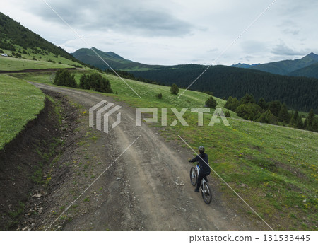 Aerial view of woman riding mountain bike on flowering grassland mountain trail Aerial view of woman riding mountain bike on flowering grassland mountain trail 131533445