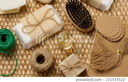 Natural handmade soap bars with various craft supplies on a woven mat. The soap bars are wrapped in burlap and twine. 131533522