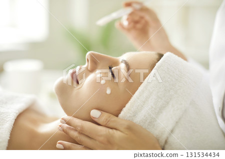 Beautician's hands applying anti-aging facial cream on woman client face in spa salon. Beautician's hands applying anti-aging facial cream on woman client face in spa salon. 131534434