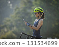 Woman cyclist using mobile phone in summer park 131534699
