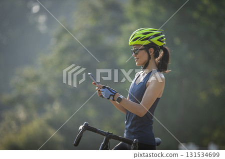 Woman cyclist using mobile phone in summer park 131534699