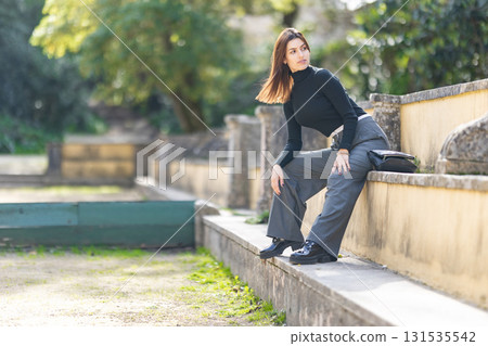 Young woman sitting outdoors looking into distance 131535542