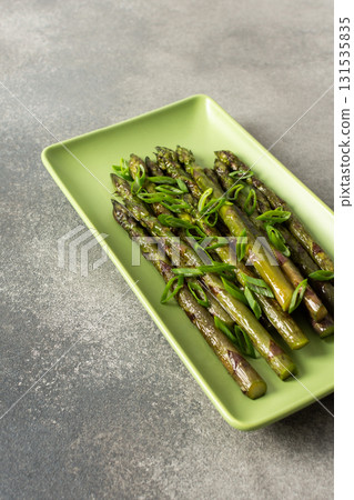 Freshly grilled asparagus topped with chopped green onions sits on a green platter in a modern kitchen. This vibrant dish showcases healthy cooking and fresh ingredients Freshly grilled asparagus topped with chopped green onions sits on a green platter in a modern kitchen. This vibrant dish showcases healthy cooking and fresh ingredients 131535835