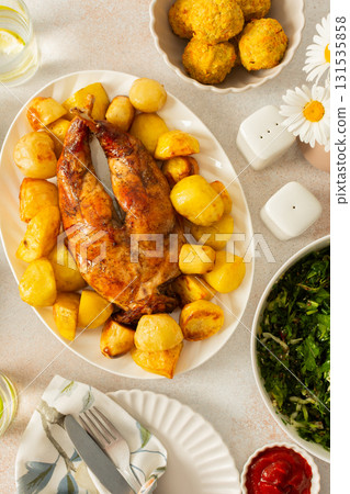 A hearty meal features a beautifully baked rabbit surrounded by golden potatoes, Accompanying the dish is a fresh salad, soft chickpea buns. This inviting setup showcases a warm dining 131535858