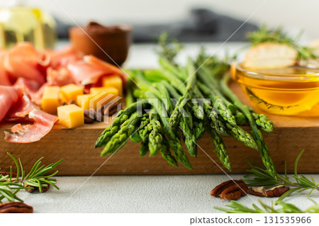 A vibrant charcuterie board is set for a gathering, showcasing fresh asparagus, assorted cheeses, cured meats, and nuts. This setup invites guests to enjoy tasty bites together A vibrant charcuterie board is set for a gathering, showcasing fresh asparagus, assorted cheeses, cured meats, and nuts. This setup invites guests to enjoy tasty bites together 131535966