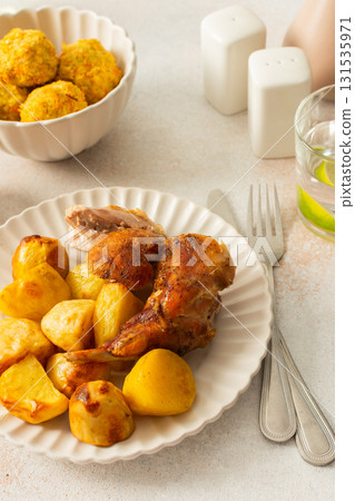 A delicious meal featuring roasted rabbit paired with golden-brown potatoes creates a hearty main course. Accompanying the dish are vibrant chickpea buns and a fresh salad 131535971