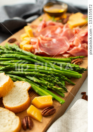 Indulge in a beautifully arranged charcuterie board with vibrant asparagus, savory cured meats, assorted cheeses, and freshly toasted bread, ideal for sharing with friends 131535972