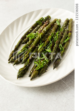 Steamed asparagus spears topped with fresh herbs are arranged neatly on a white plate. The dish appears vibrant and is suitable for a healthy meal or side 131536008